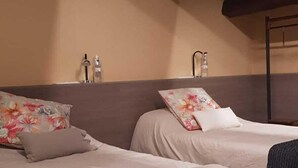 A room with two beds, wooden beams on the ceiling, and a beige wall.