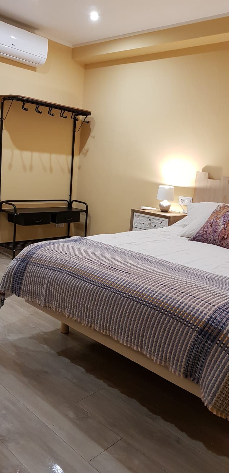 A hotel room with a bed, bedside table, lamp, and a standing heater.