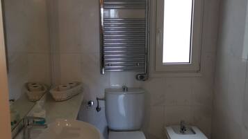 A bathroom with a sink, toilet, and bidet. There is a mirror above the sink and a window above the toilet.