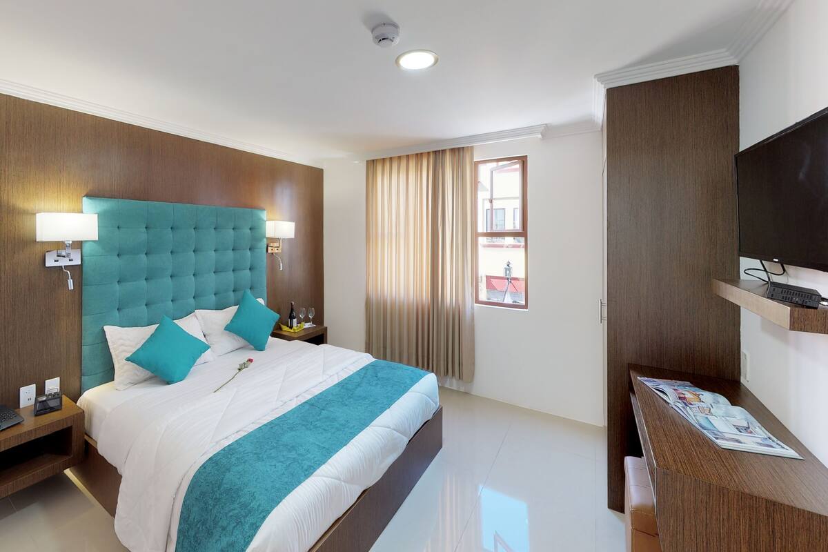 A hotel room with a bed, a desk, a television, and a window with curtains.