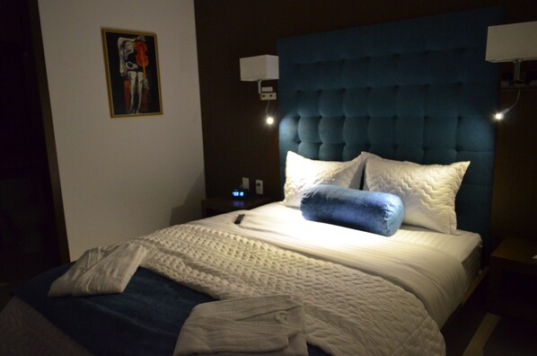 Una cama bien hecha con cabecera azul, ropa de cama blanca y una sola almohada.