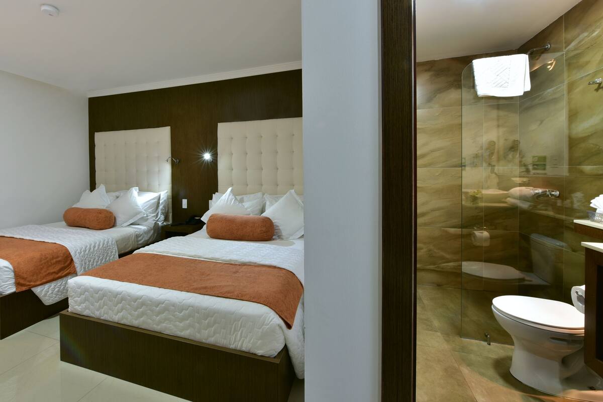 A hotel room with two beds, a large mirror, and a modern bathroom with a glass shower enclosure.