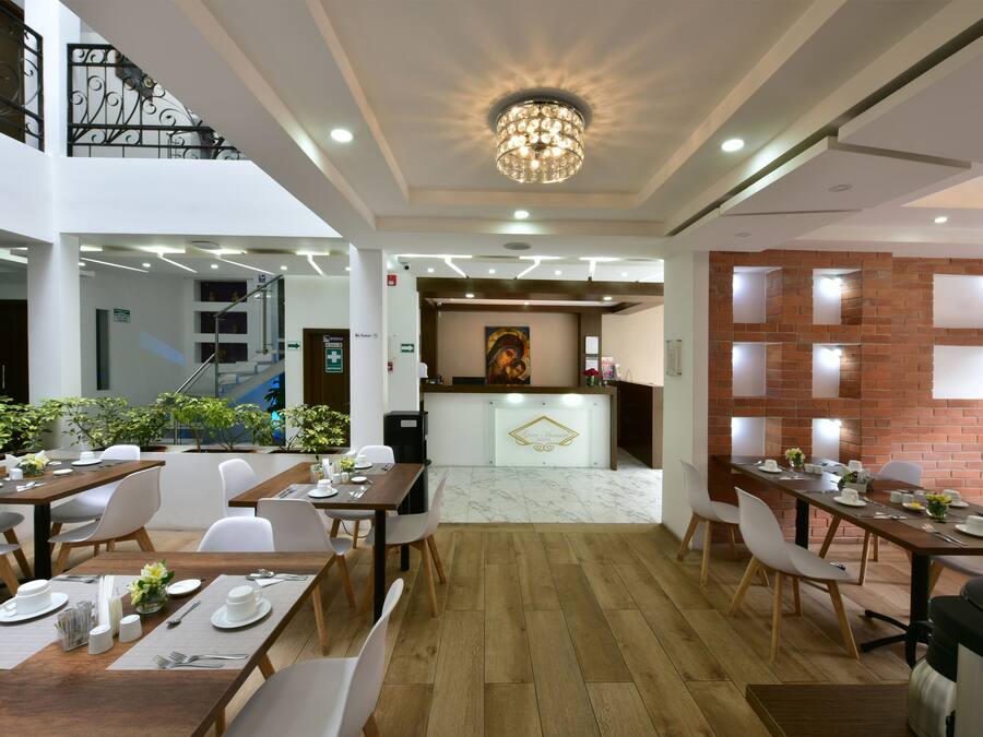 Un comedor moderno con mesas de madera y sillas blancas, un mostrador de recepción y una escalera.