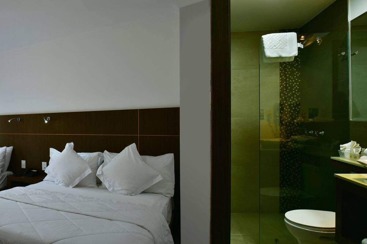 A hotel room with two beds, a dining area with blue chairs, and a bathroom with a glass shower.