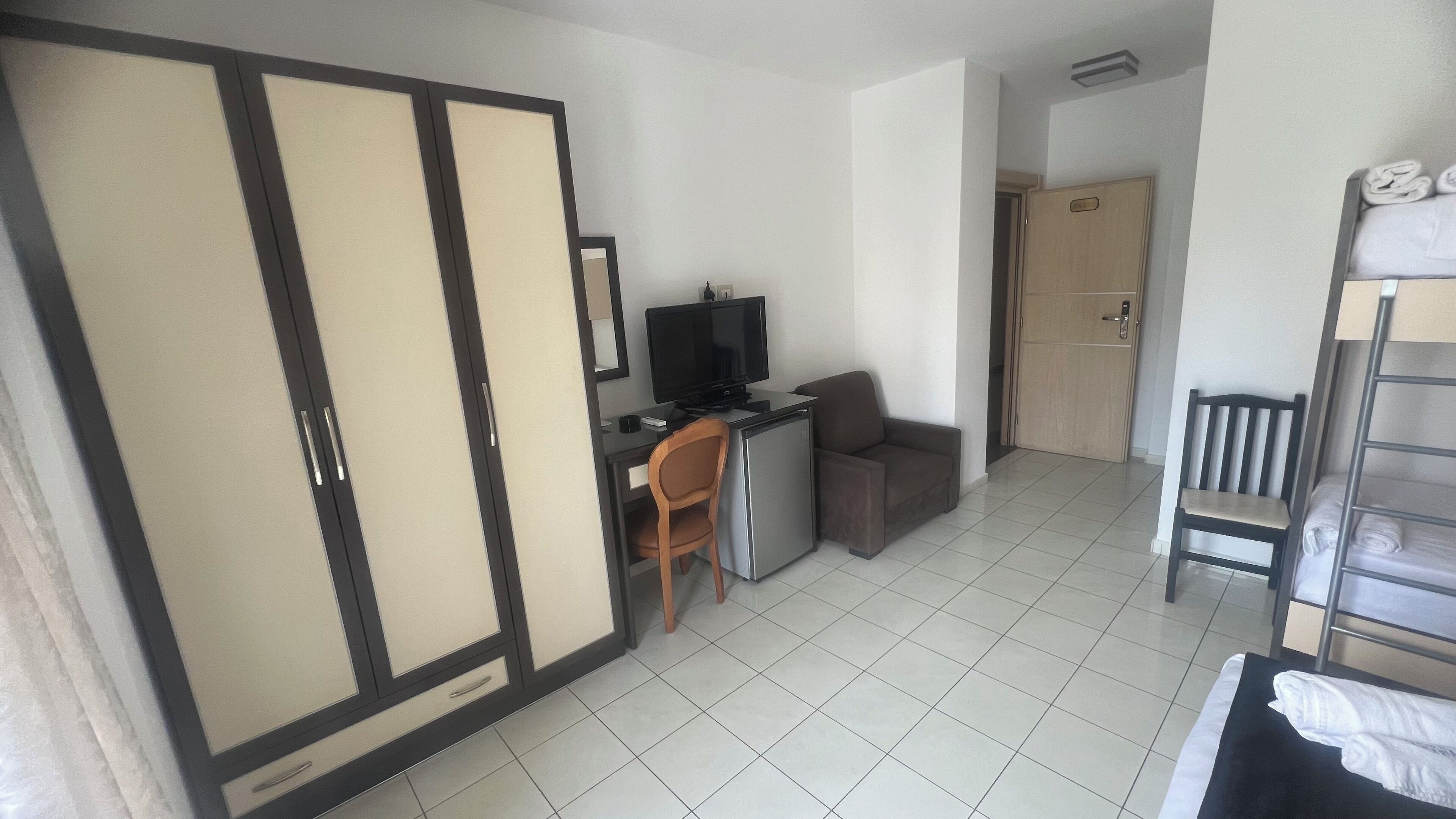 Habitación de hotel con cama, escritorio, computadora, televisor, silla y armario.