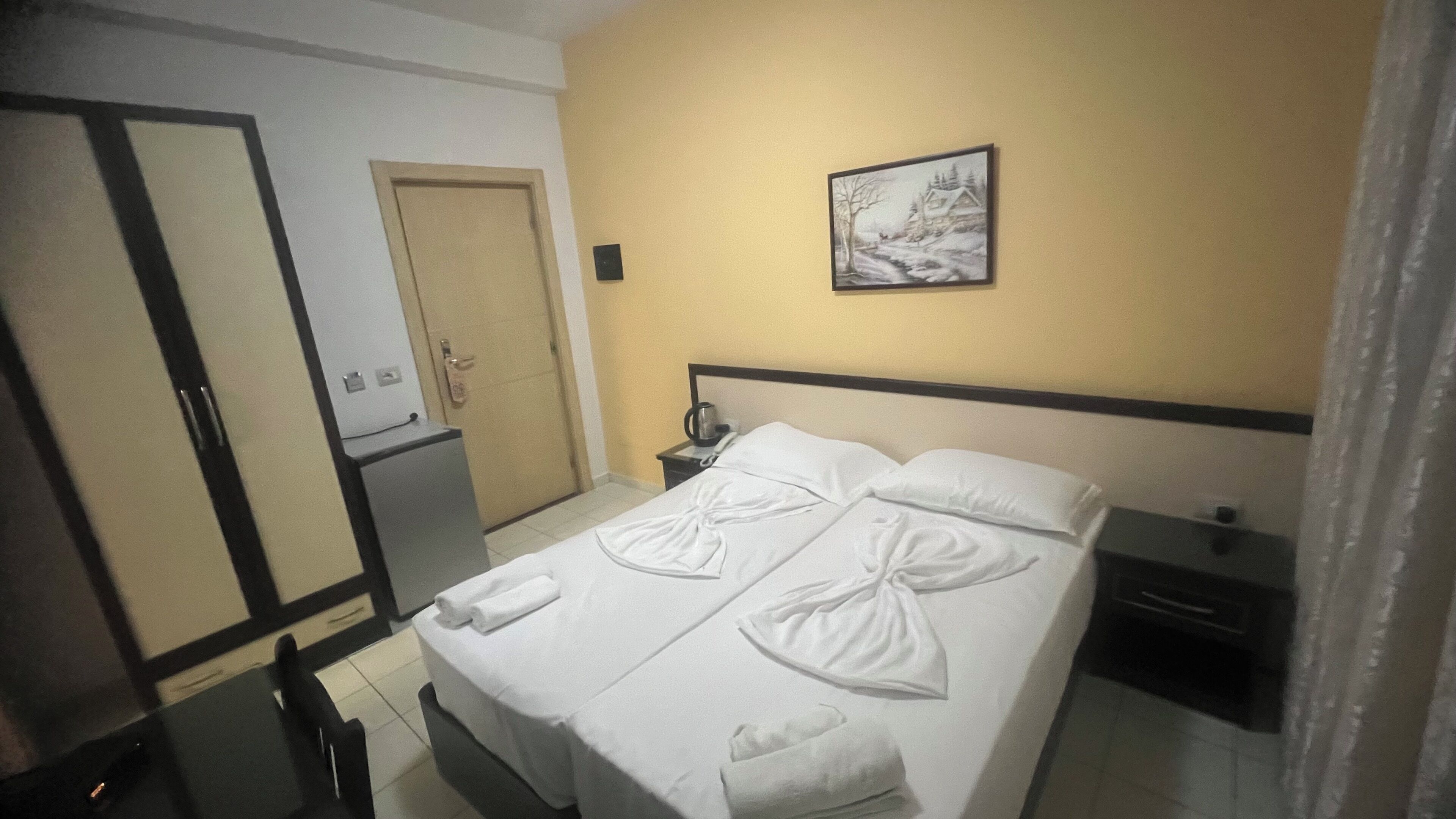 Een hotelkamer met een bed, nachtkastje, bureau, kledingkast en een deur.
