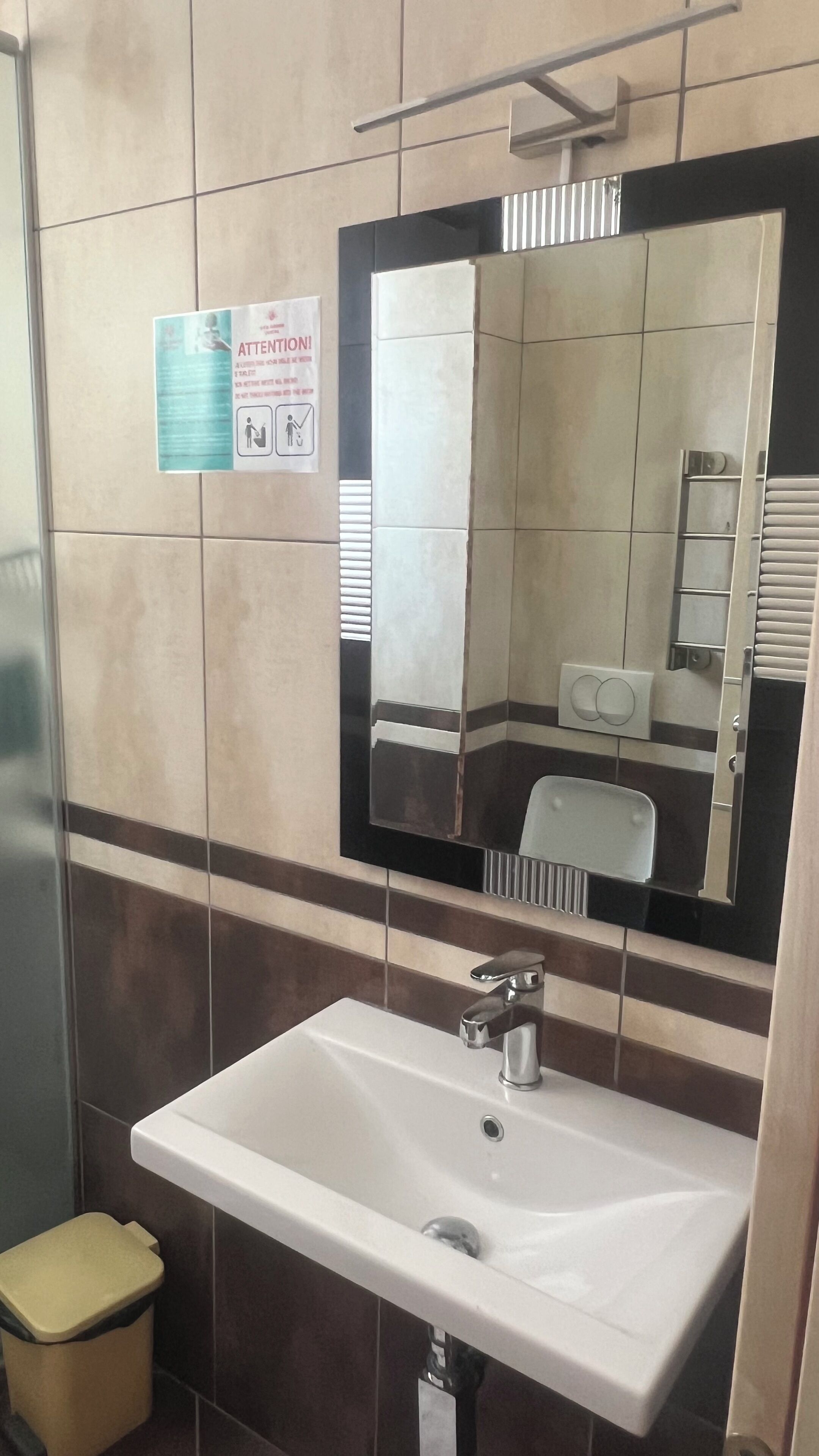 A bathroom with a white sink, a mirror, and a trash bin.