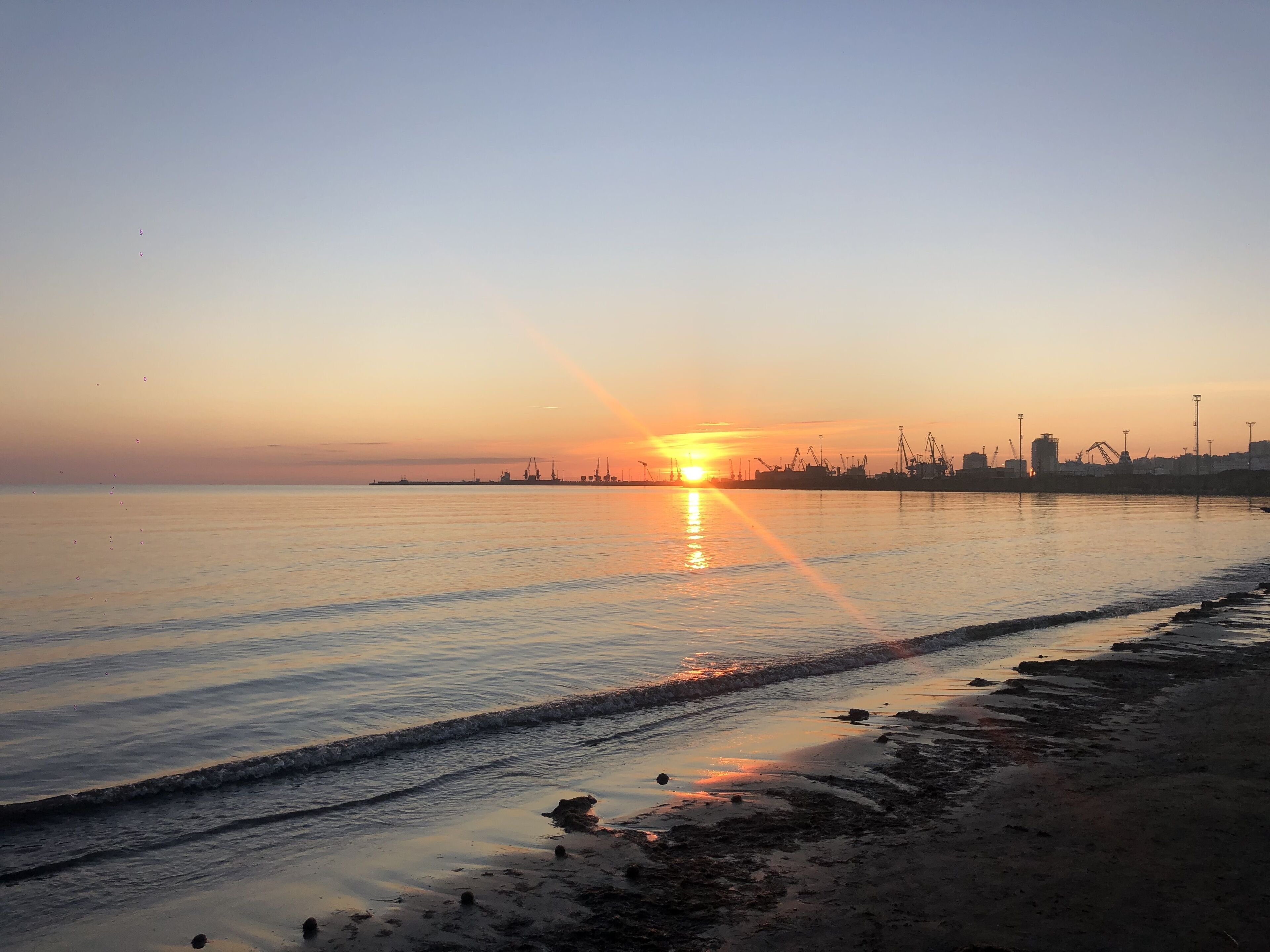Un coucher de soleil sur une mer calme, avec une côte lointaine à l’horizon.