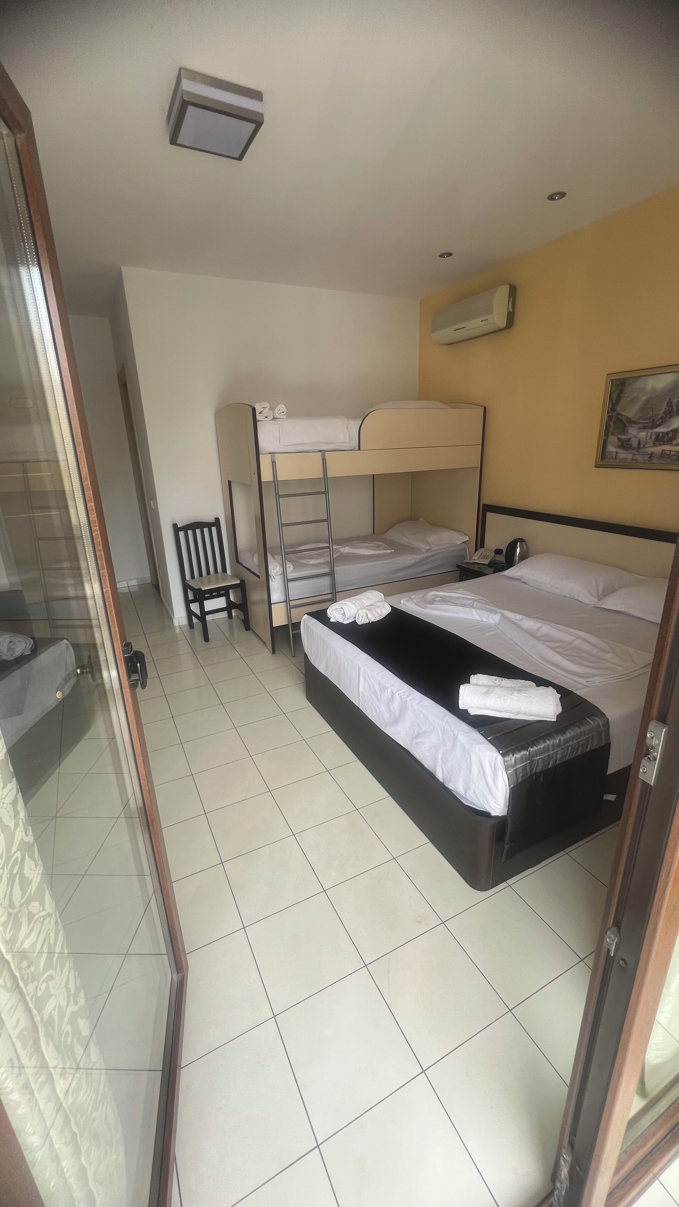 A hotel room with a bunk bed, a single bed, a chair, a desk, and a window.