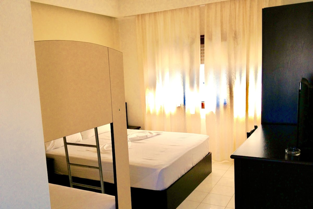 A hotel room with a bunk bed, a desk, and a TV.