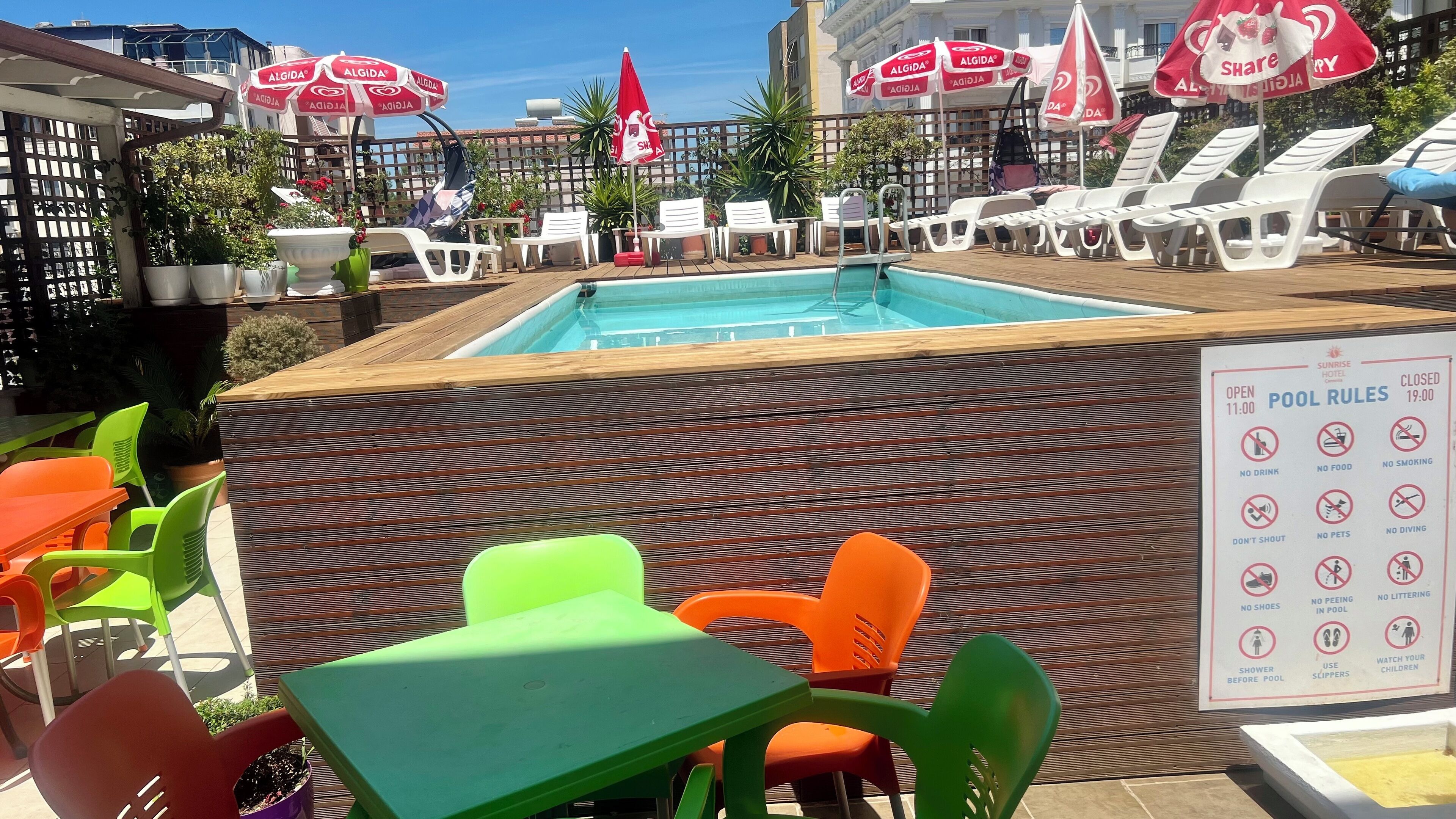 Ein Poolbereich mit Liegestühlen und Sonnenschirmen, einer Holzterrasse und einem Schild mit Poolregeln.