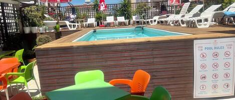 Ein Poolbereich mit Liegestühlen und Sonnenschirmen, einer Holzterrasse und einem Schild mit Poolregeln.