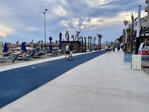 A beachside promenade with sun loungers, umbrellas, and palm trees. - Sunrise Hotel Çameria (Durrës)