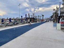 Eine Strandpromenade mit Liegestühlen, Sonnenschirmen und Palmen.