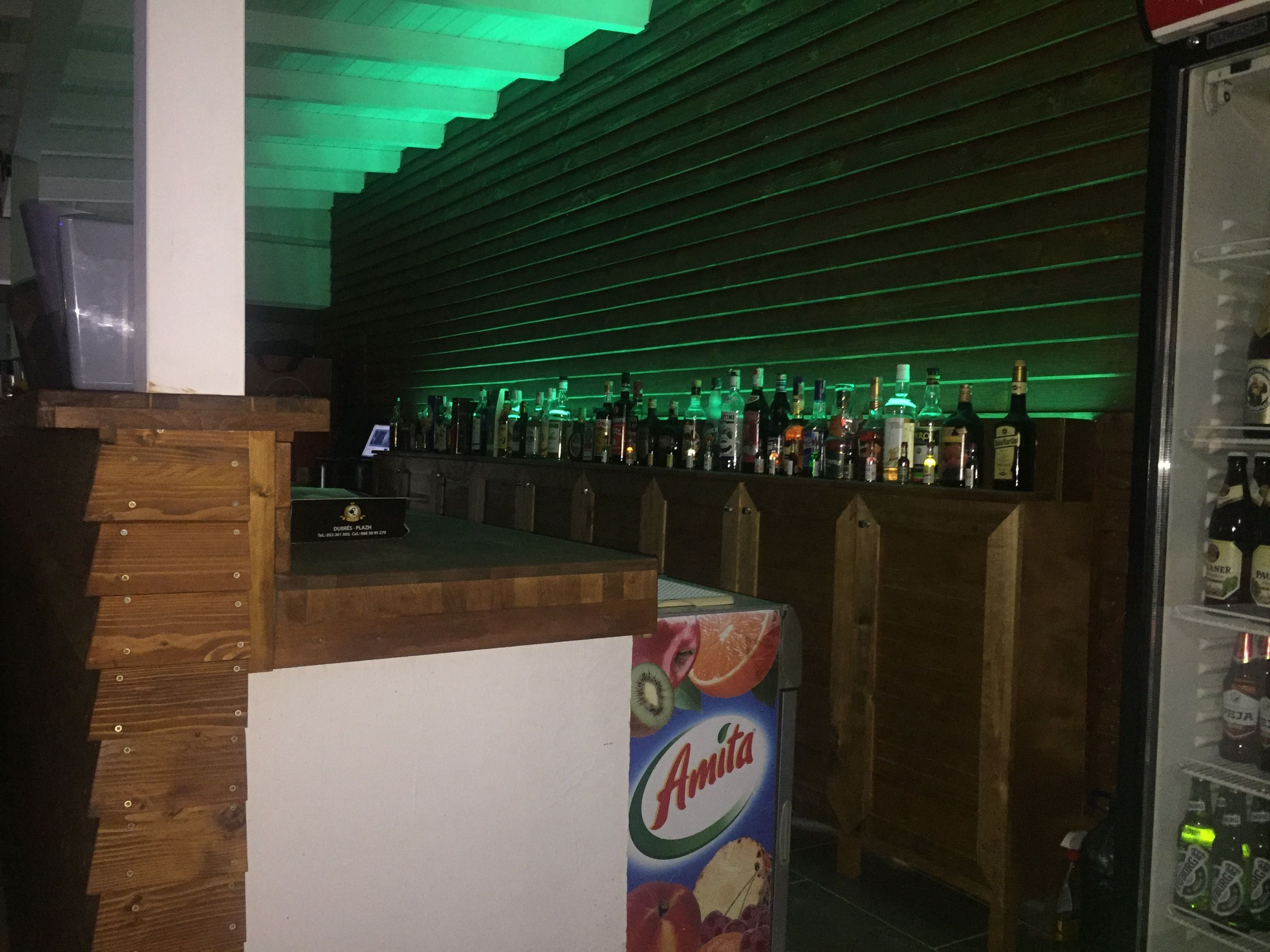 A bar area with wooden paneling, a counter with a computer, and a refrigerator stocked with beverages.