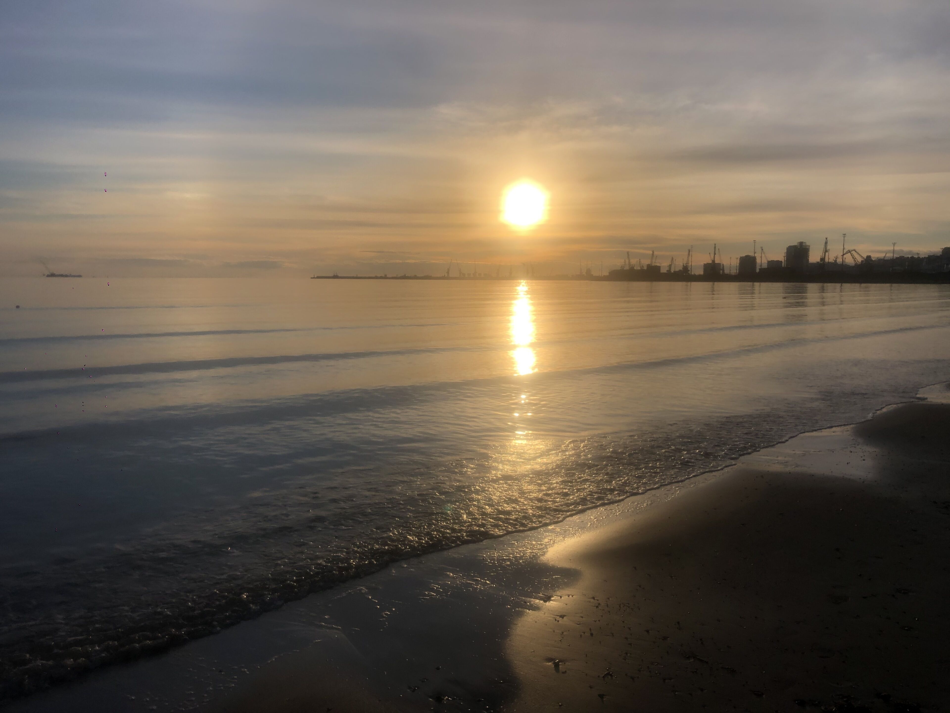A beach with a calm sea, a visible shoreline, and distant industrial structures.