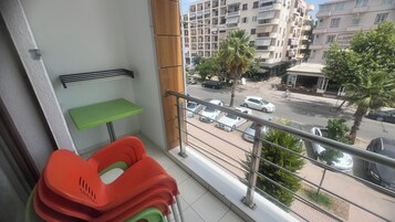A balcony with a green table and red chairs, overlooking a street with cars and buildings.