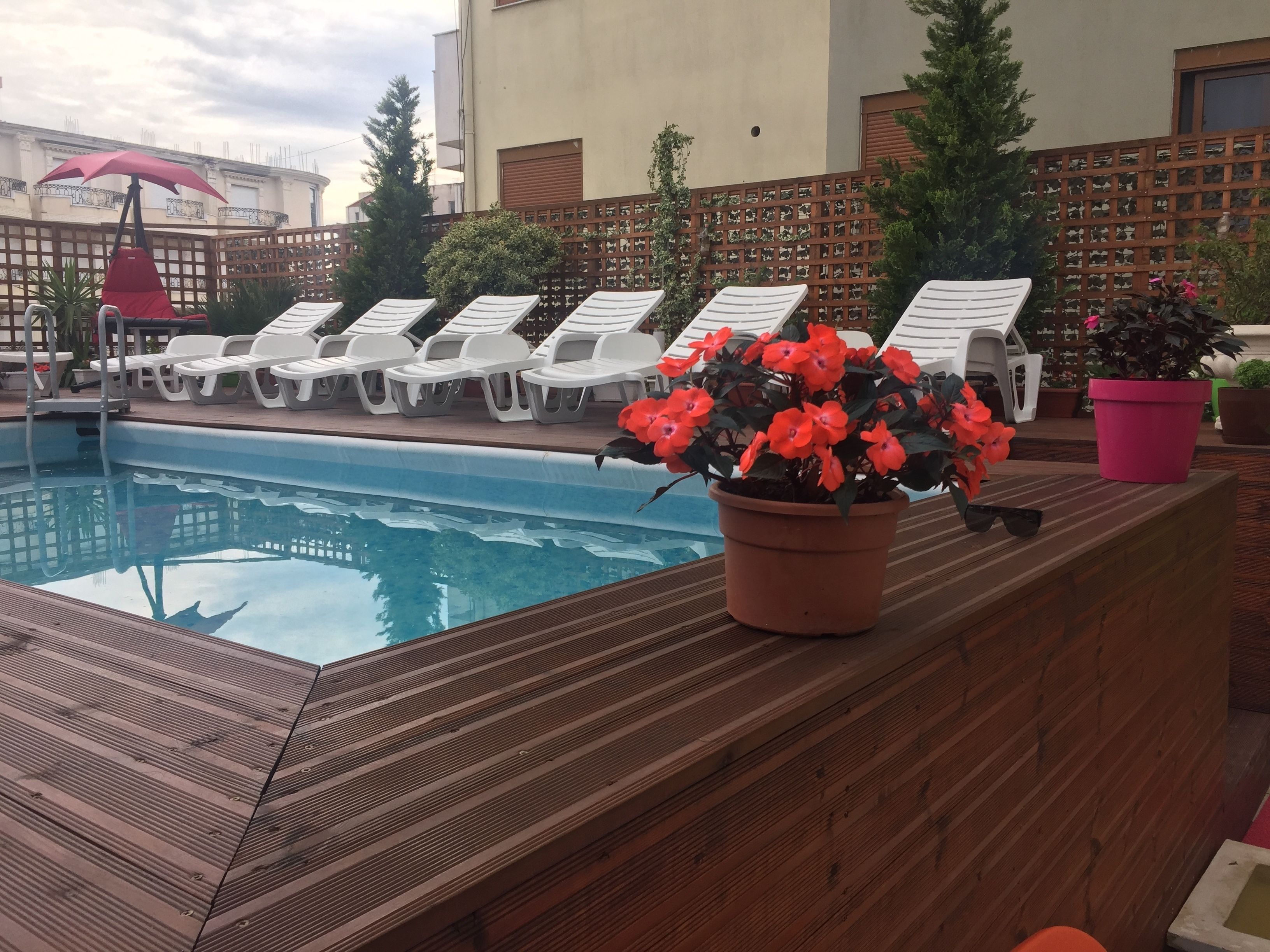 A poolside area with lounge chairs, a wooden deck, and a potted plant with flowers.