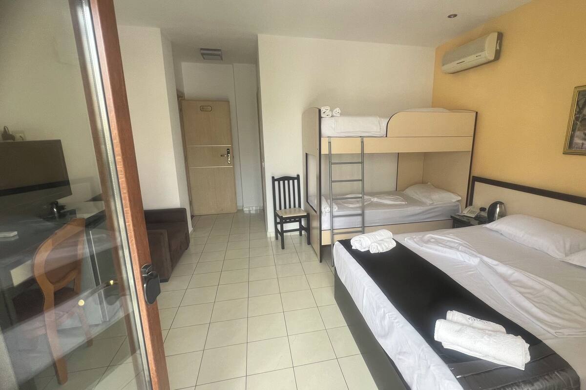 A hotel room with bunk beds, a desk with a chair, a desk lamp, a telephone, and a painting on the wall.