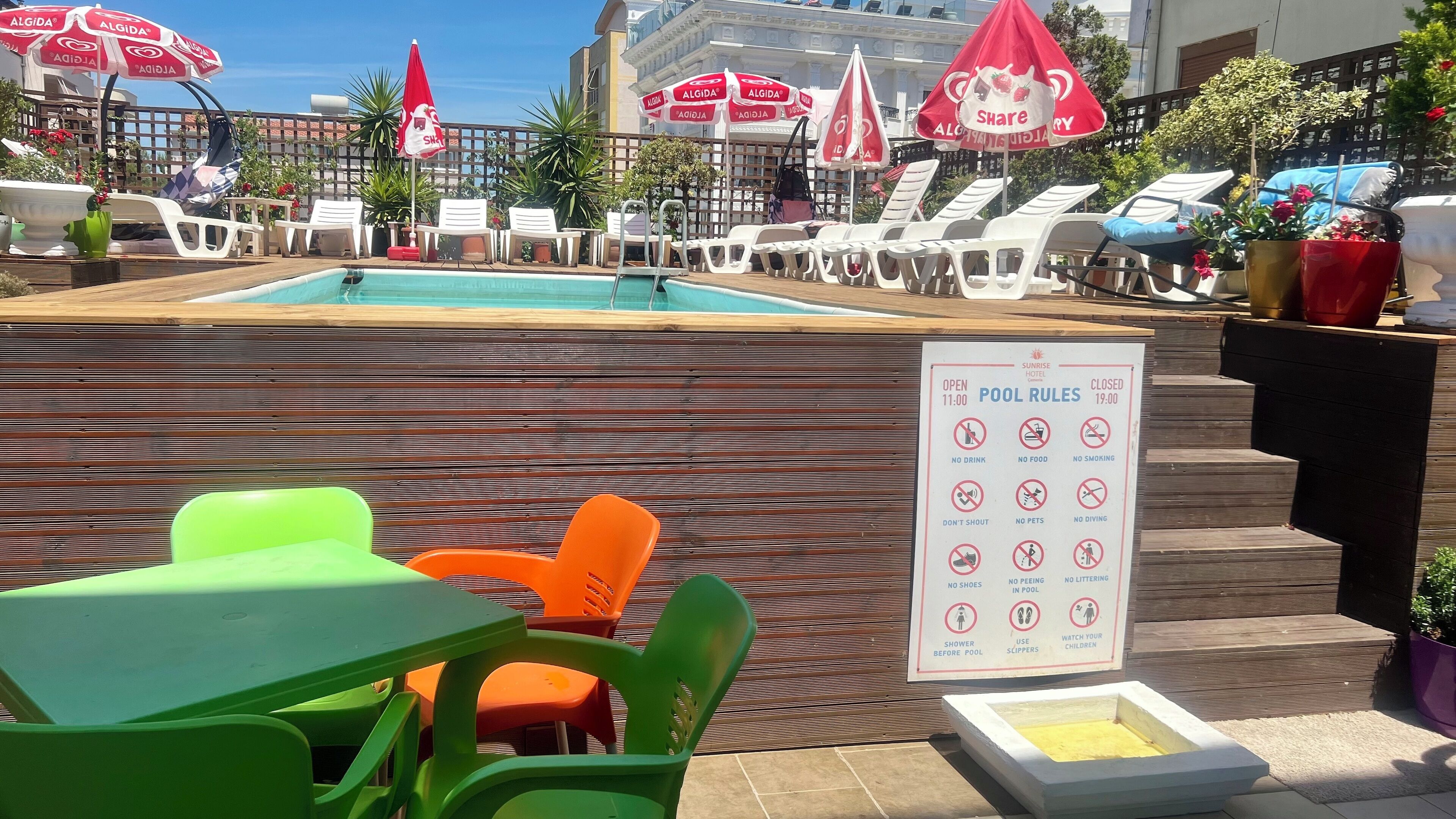A pool area with lounge chairs, umbrellas, and a pool rules sign.