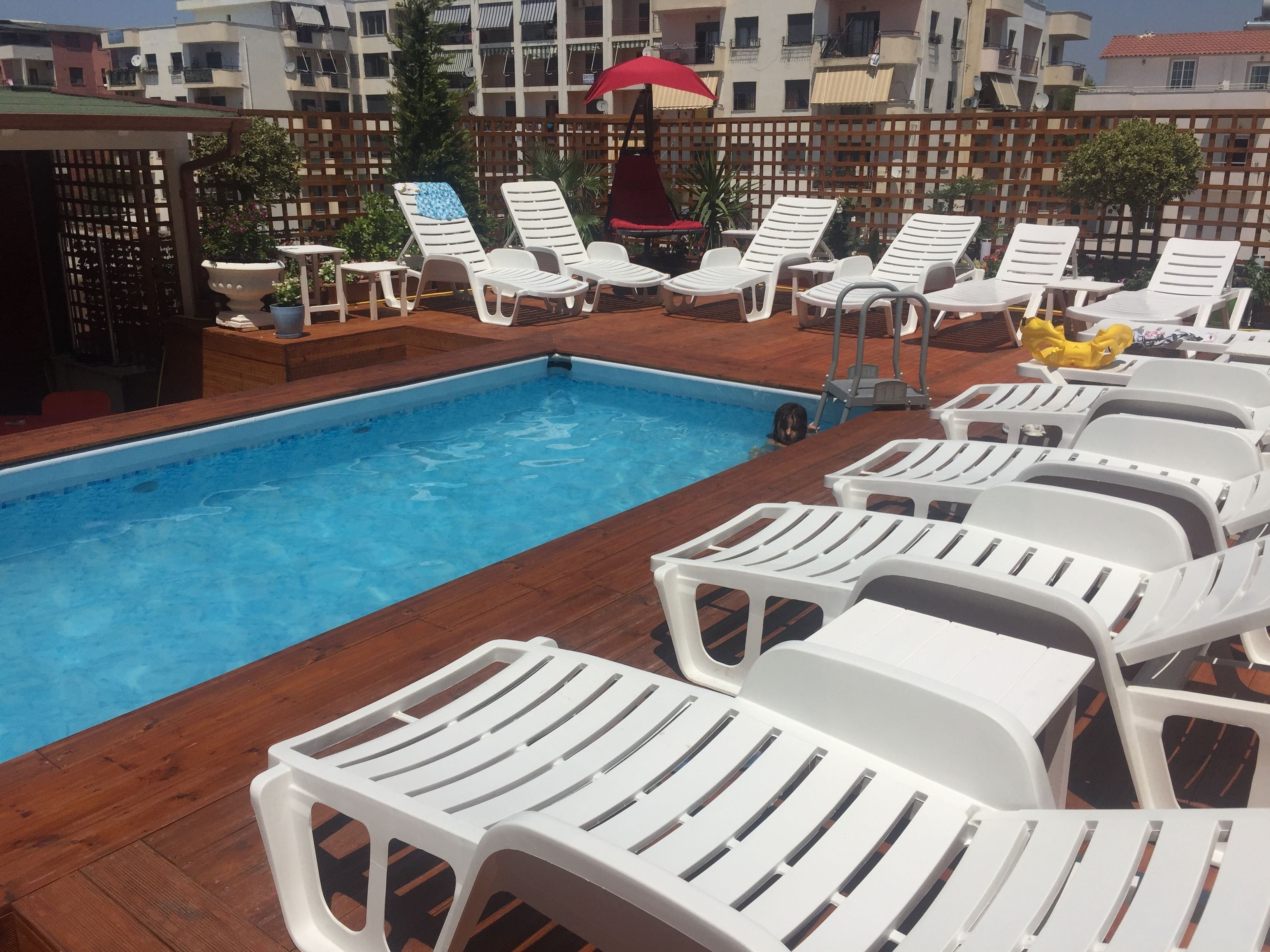 Une piscine entourée de chaises longues blanches et d’une terrasse en bois.