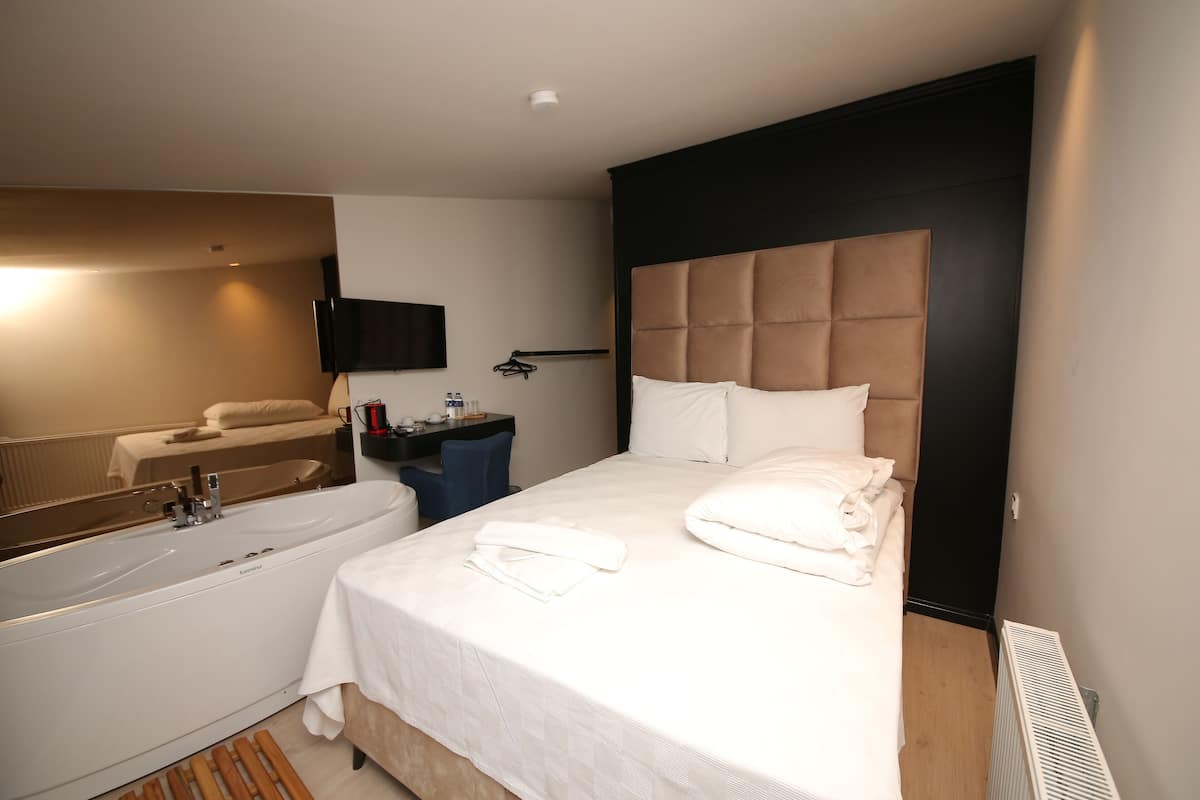 Quarto de hotel com uma cama grande, banheiro separado com banheira, televisão de tela plana na parede e uma pequena escrivaninha com cadeira.