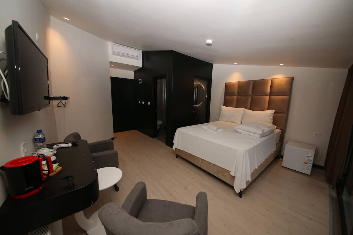 Quarto de hotel com cama, escrivaninha com chaleira, cadeira, televisão e mini-geladeira.