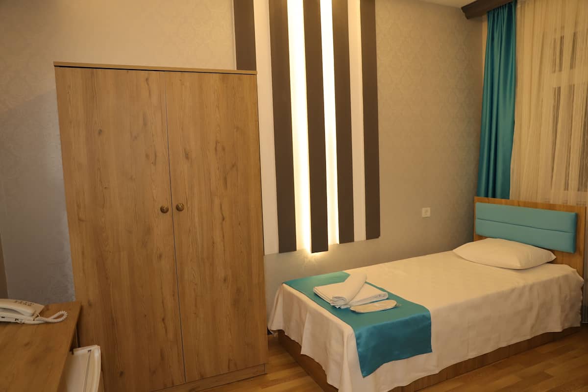Quarto com guarda-roupa de madeira, cama com colcha azul e mesa de cabeceira com telefone.