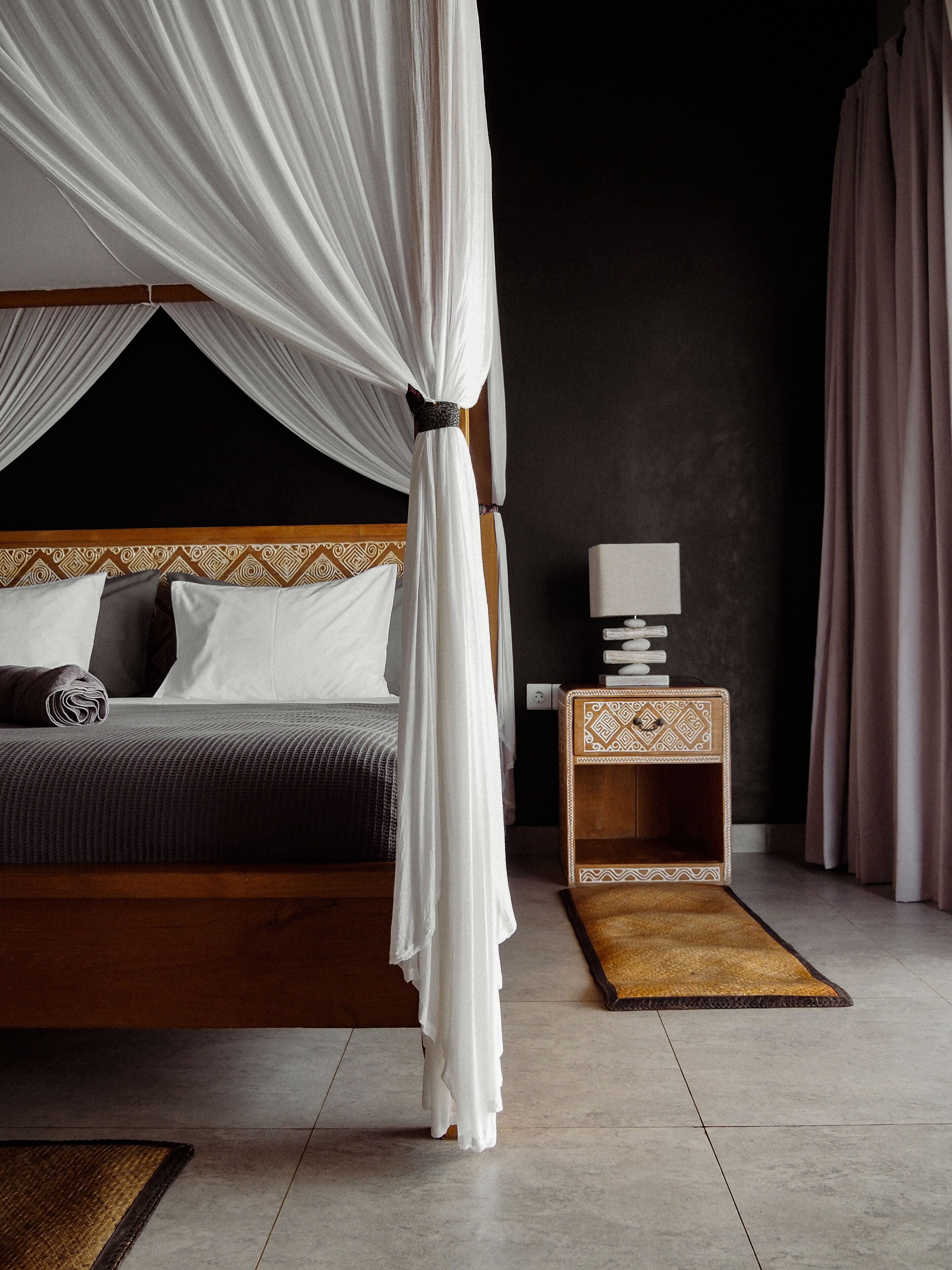 A bedroom with a four-poster bed, a bedside table with a lamp, and a small rug.