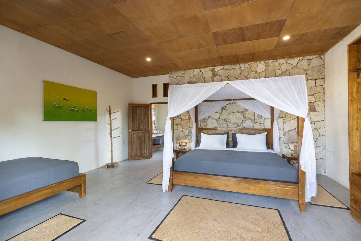 A bedroom with a four-poster bed, a smaller bed, a stone wall, and a painting on the wall.