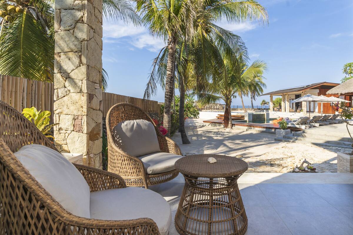 A beachside patio with wicker furniture, a stone pillar, and a view of the ocean.