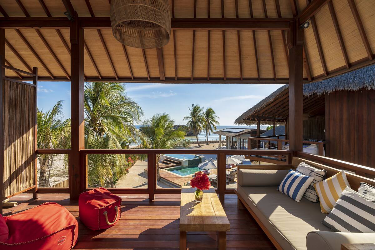 A wooden deck with a sofa, a small table with a vase, and a red bag.