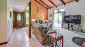 A cozy living room with a sofa, coffee table, and TV, wooden beams on the ceiling, and a door with a glass panel. - New Hampshire Vacation Rental - Walk to Beach! (Madison)