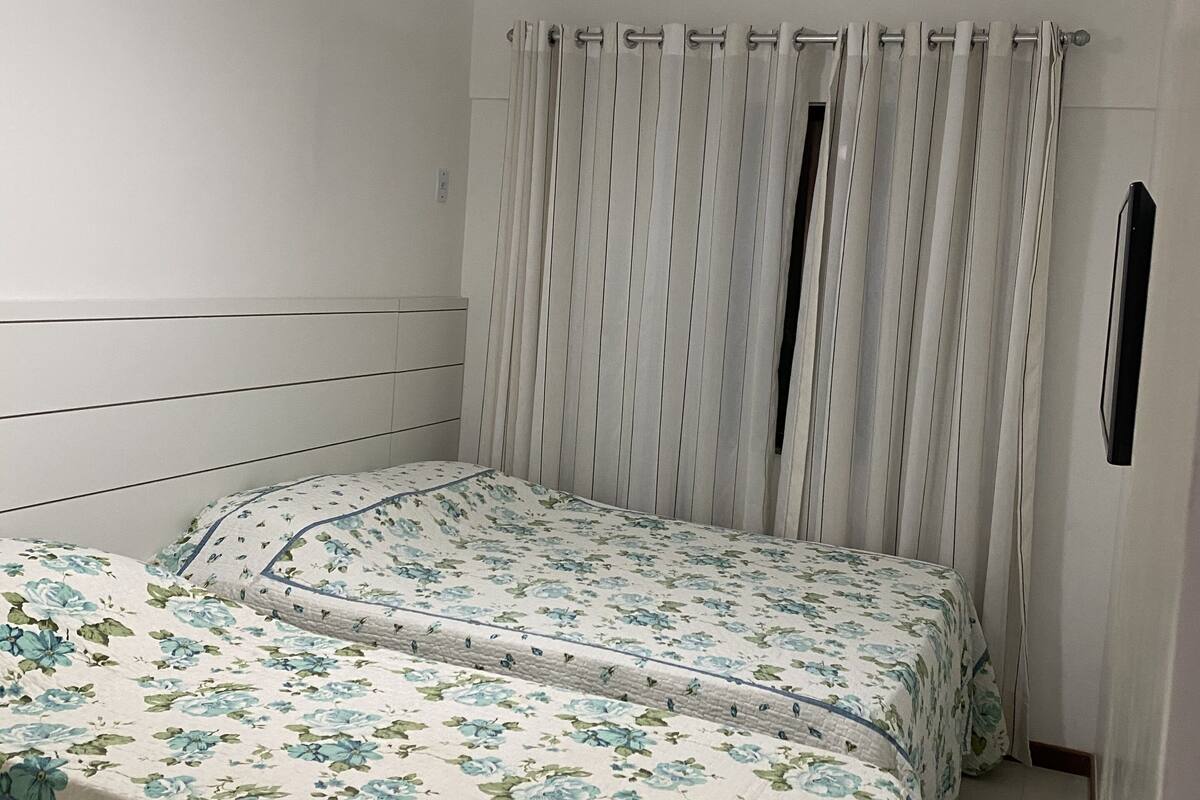 Un dormitorio con dos camas, ventilador de techo, cortinas blancas y unidad de aire acondicionado.