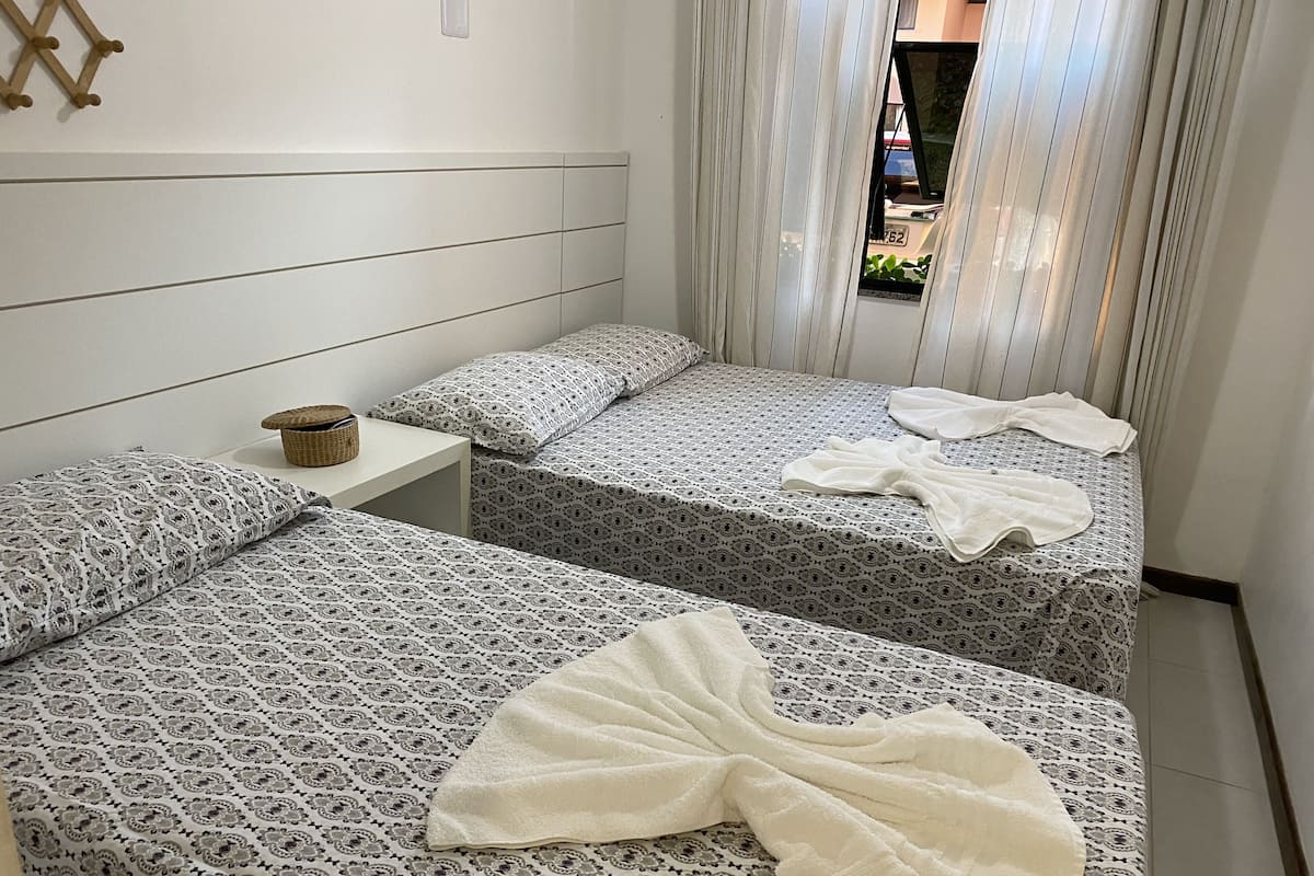 Una habitación de hotel con dos camas, una mesita y una ventana con cortinas.