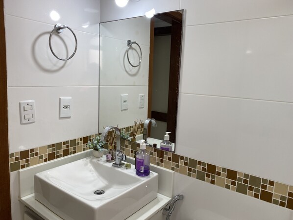 A bathroom with a white sink, a mirror, a towel ring, a shower, and a tiled backsplash.