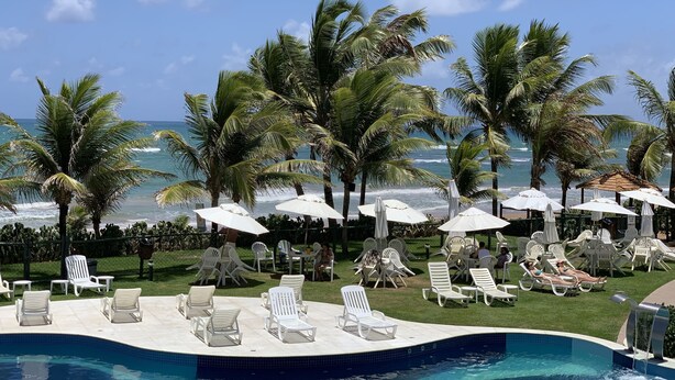 Zona de piscina con sillones de descanso y sombrillas, con vistas al océano.