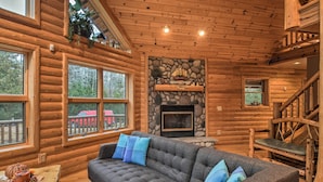 A log cabin interior with a stone fireplace, a sofa with blue cushions, and a wooden staircase.