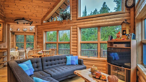 A cozy log cabin interior with a sectional sofa, wooden dining table, and a television.