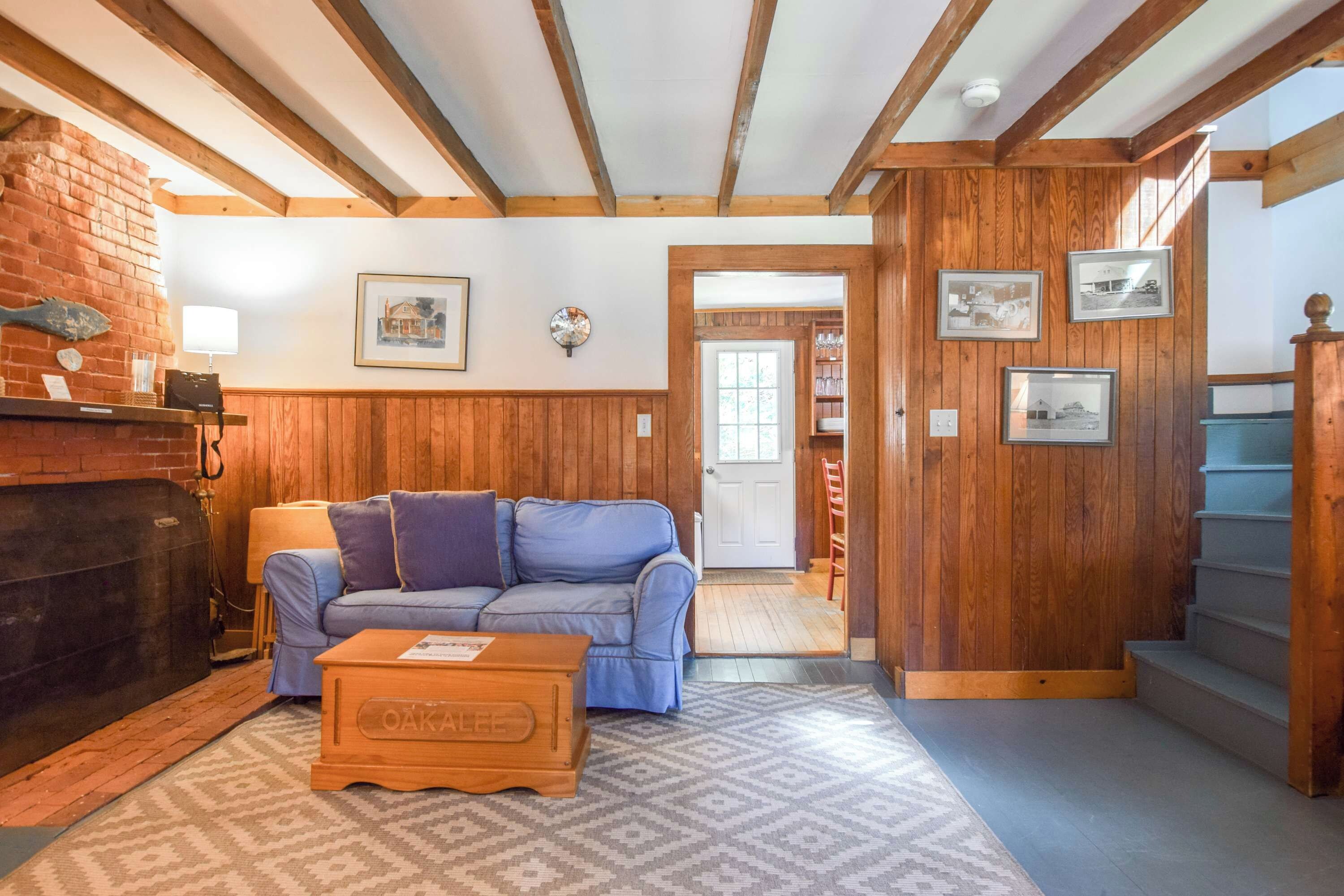 A cozy living room with a blue sofa, wooden walls, a fireplace, and a staircase.