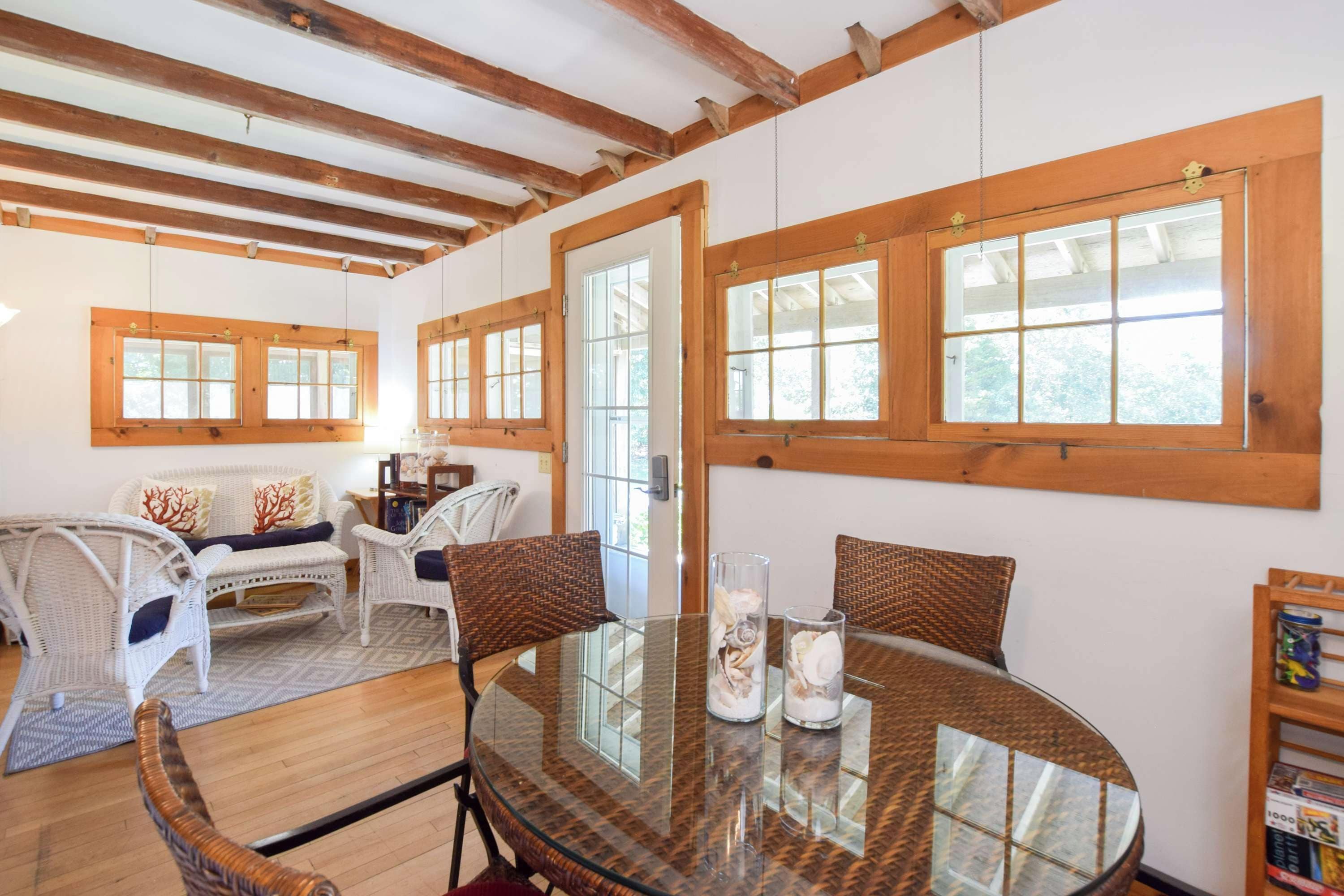 A room with a glass table, wicker chairs, a sofa, and wooden beams on the ceiling.
