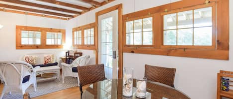 A room with a glass table, wicker chairs, a sofa, and wooden beams on the ceiling.