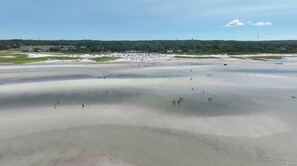 Ampla faixa de areia com pessoas espalhadas pela praia e pelo mar.