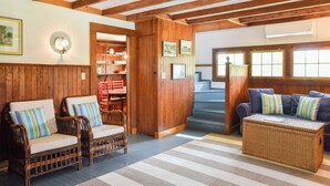 Ein gemütliches Zimmer mit Holzwänden und -decke, Korbmöbeln und einer Treppe, die zu einer weiteren Ebene führt.