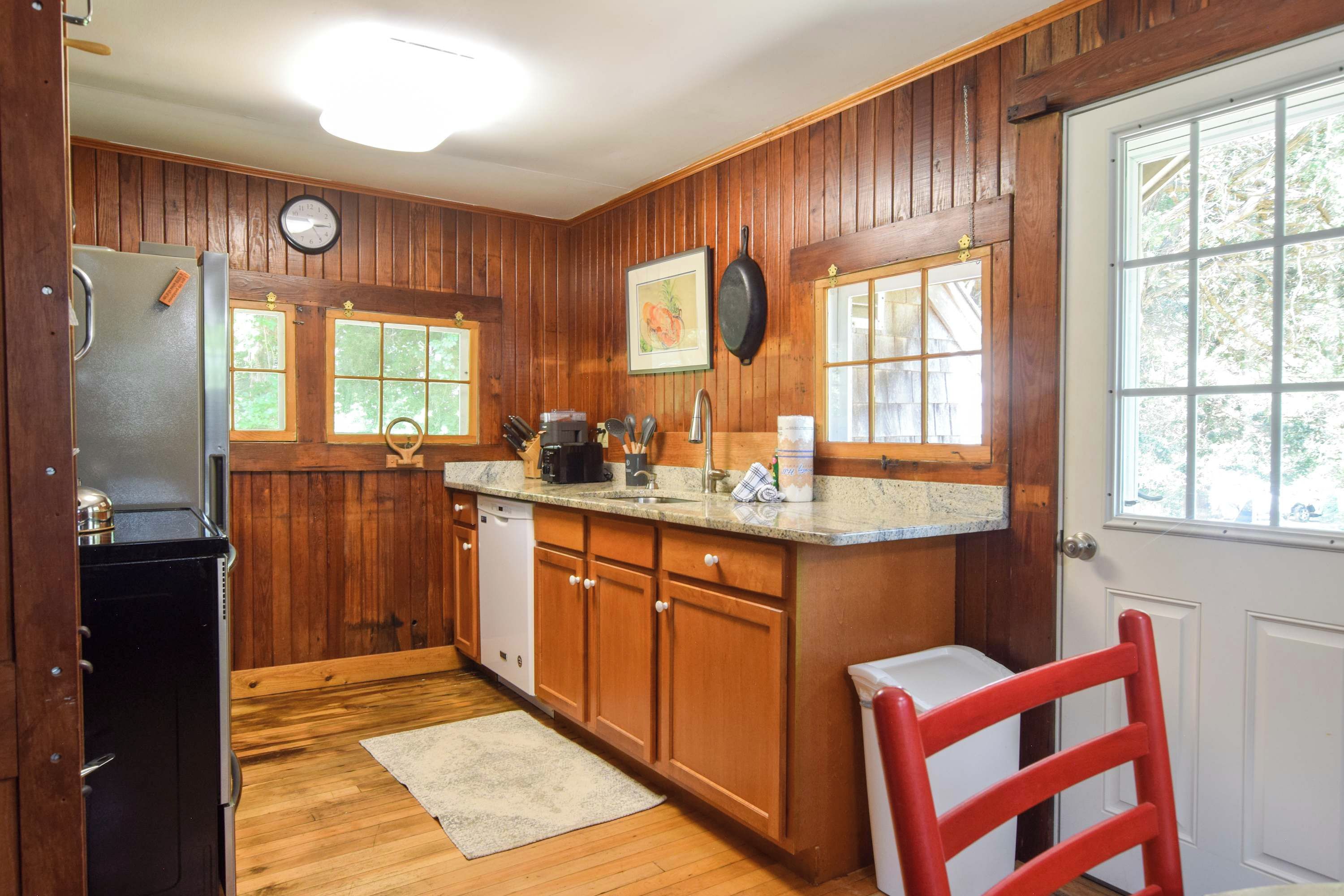 A kitchen with wooden paneling, a refrigerator, a dishwasher, a sink, and a window with a view of trees.