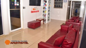 A hotel lobby with a reception desk, a red leather sofa, a minibar, and a glass door leading to the outside.