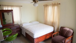 A hotel room with a bed, a chair, a desk with a mirror, and a ceiling fan.