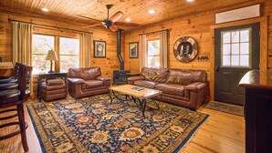 A cozy log cabin interior with leather furniture, a central rug, and a wood-paneled ceiling. - 25-Acre Mountain Retreat w/ Trails, Pond, Hot Tub (Penrose)