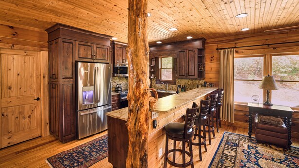 A wooden interior with a central island, bar stools, and a large window. - 25-Acre Mountain Retreat w/ Trails, Pond, Hot Tub (Penrose)