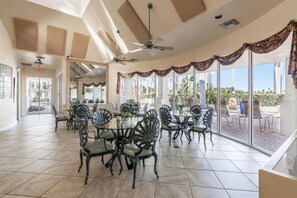 A spacious indoor area with a high ceiling, large windows, and a dining setup with chairs and tables.